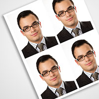 identite Quatre photos d'identité identiques, au format passeport, d'un homme aux cheveux courts et foncés, portant des lunettes rectangulaires, un costume sombre, une chemise à rayures claires et une cravate, sont disposées selon une grille 2x2 sur une feuille blanche inclinée. Ces images professionnelles mettent en valeur le savoir-faire de qualité typique de Photographe Genève.
