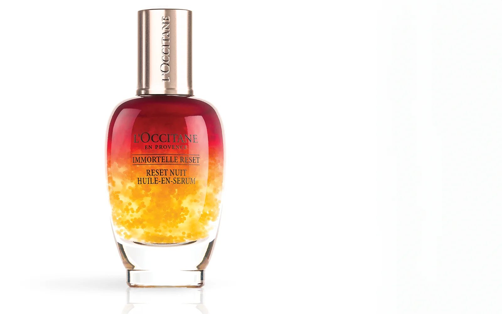 Un flacon en verre du sérum de nuit Immortelle Reset de L'Occitane, avec un motif dégradé allant du jaune à la base au rouge profond au sommet, avec des accents dorés et du texte sur le devant, sur un fond blanc.