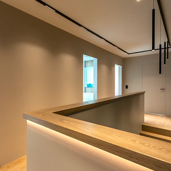 Un couloir intérieur moderne au design minimaliste, aux murs beiges et aux rampes en bois, photographié par Photographe Geneve, est doté d'un éclairage encastré et de fenêtres verticales qui laissent entrer la lumière naturelle.