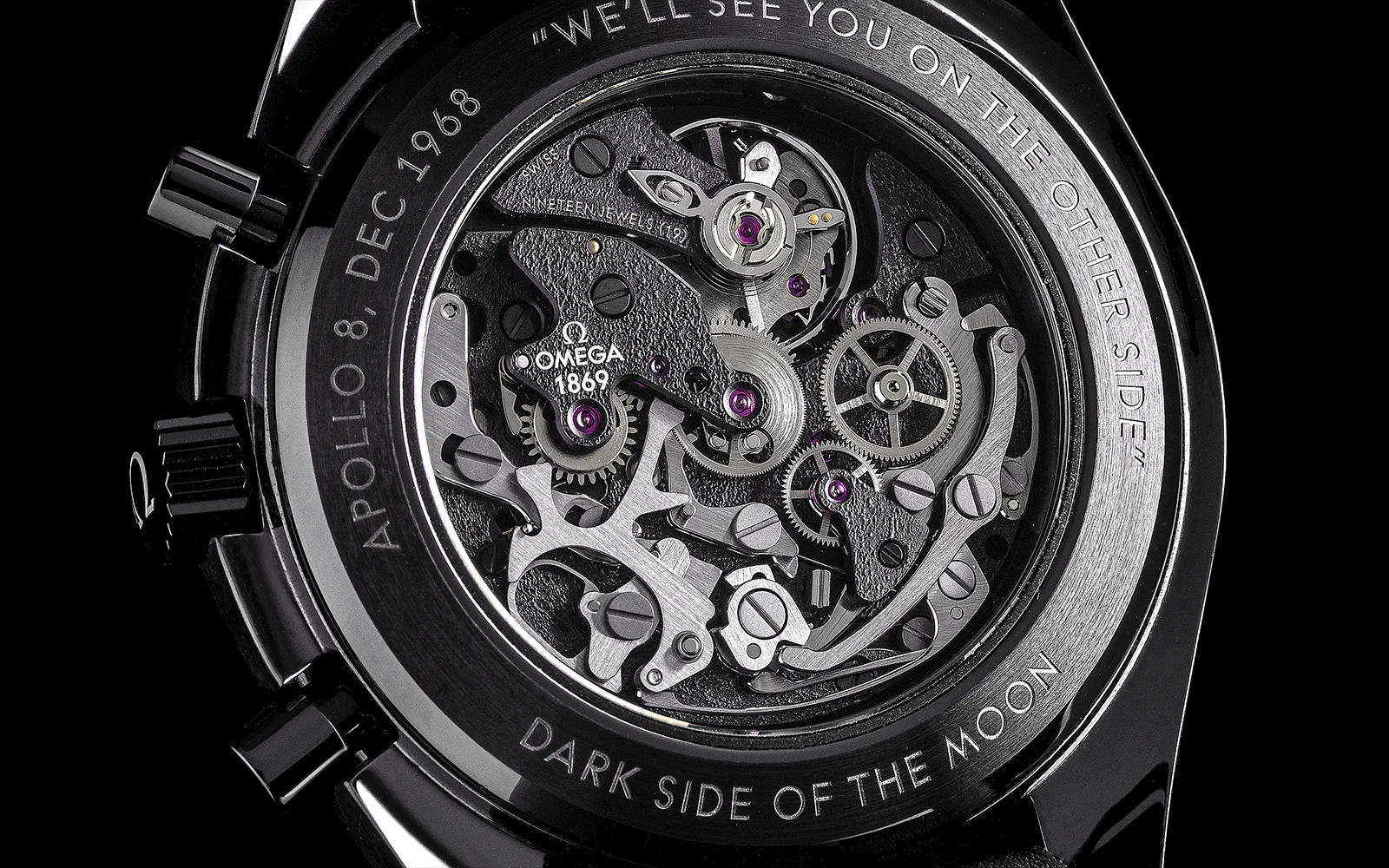 Gros plan sur le dos d'une montre Omega, montrant des mouvements mécaniques complexes. Le texte gravé indique "APOLLO 8 DEC 1968", "WE'LL SEE YOU ON THE OTHER SIDE" et "DARK SIDE OF THE MOON".